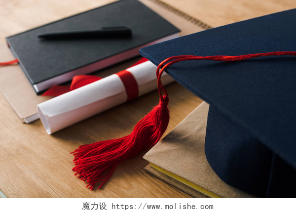 桌子上的博士帽和毕业证带有木制背景的钢笔、文凭和毕业帽的笔记本的选择性焦点